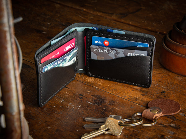 Bucklaw bifold wallet in black - laying on rustic table 