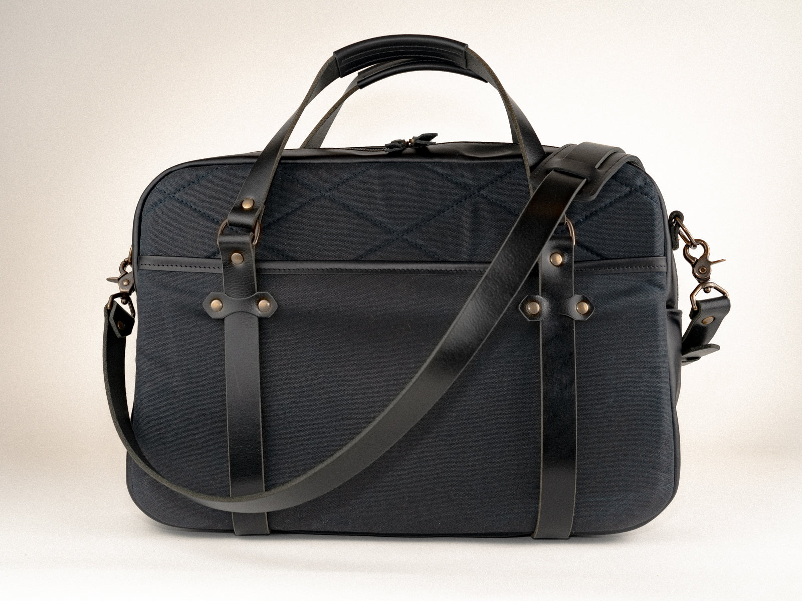 quilted side of the campbellton laptop bag in black canvas with black leather accents, and a cross-body strap draped over the corner.