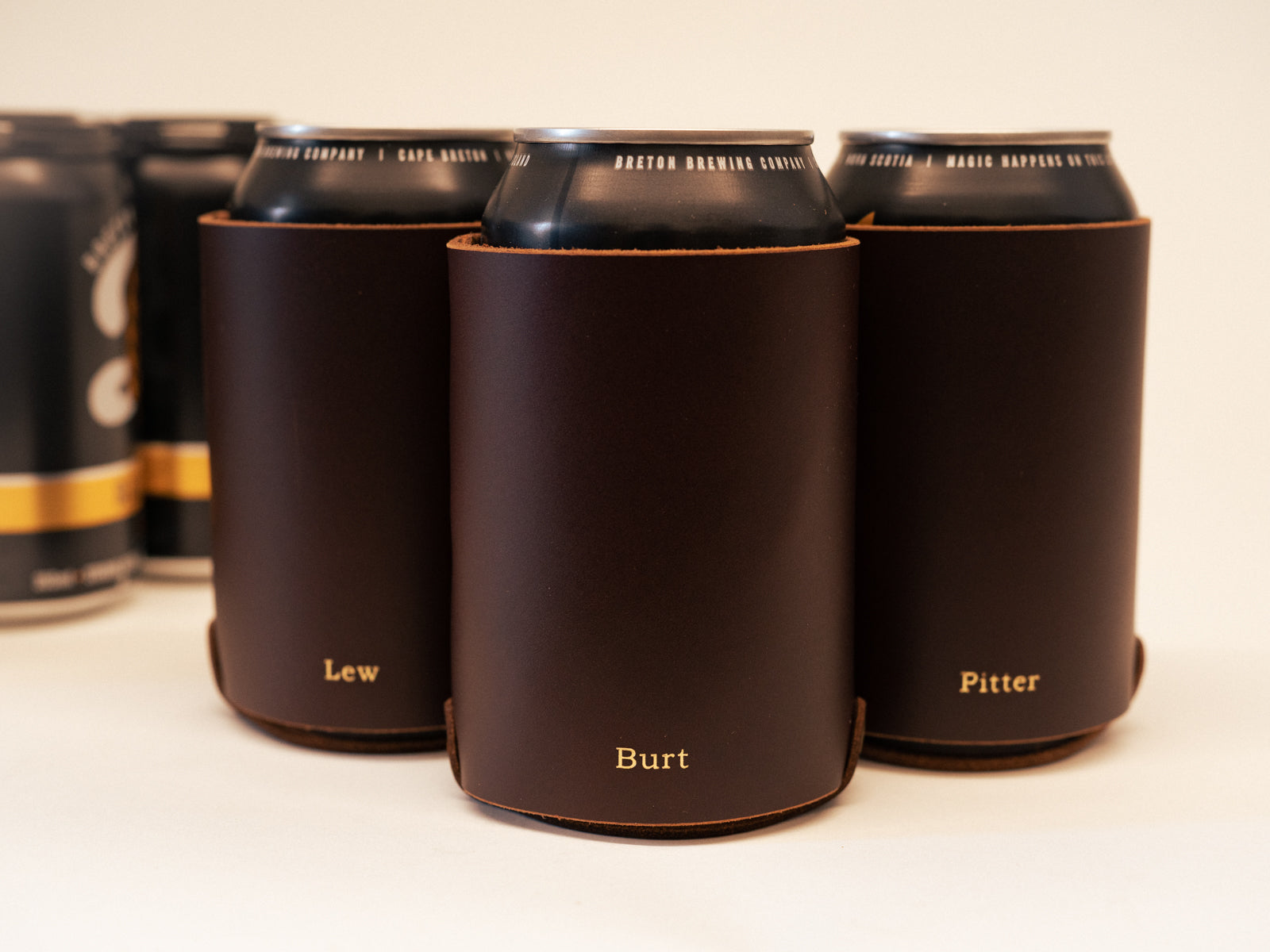 Brown leather can coozies on table, embossed with nicknames in gold foil