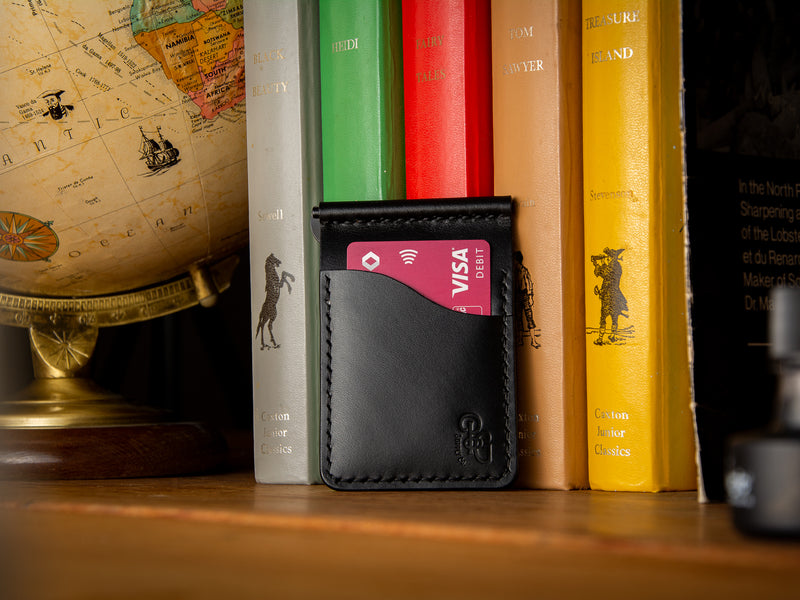 Dunvegan money clip card wallet in black sitting on a shelf of books