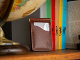 Dunvegan money clip card wallet in brown sitting on a shelf of books