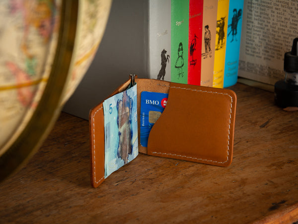 Dunvegan money clip card wallet in full grain tan leather sitting on a shelf of books