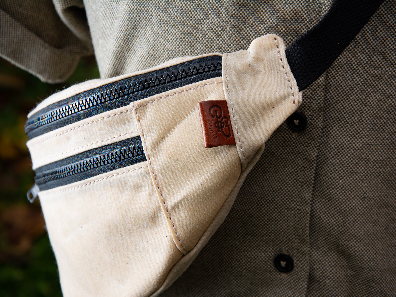 Detail shot of cream waxed canvas franey fanny pack, showing leather tax, cotton webbing strap and black zipper
