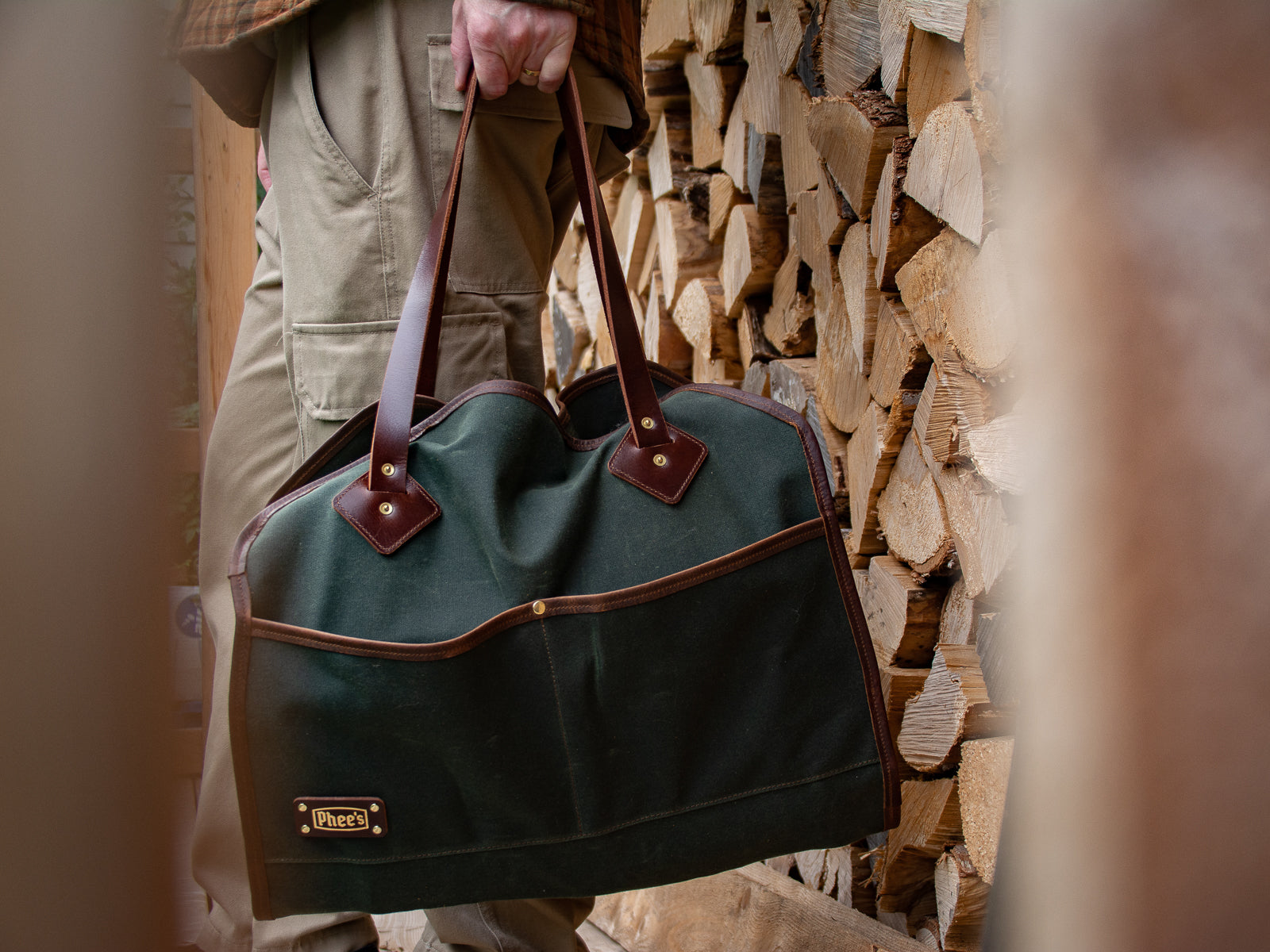 A person with their waxed canvas glen morrison log carrier in olive with brown leather straps stocked up with wood for winter!