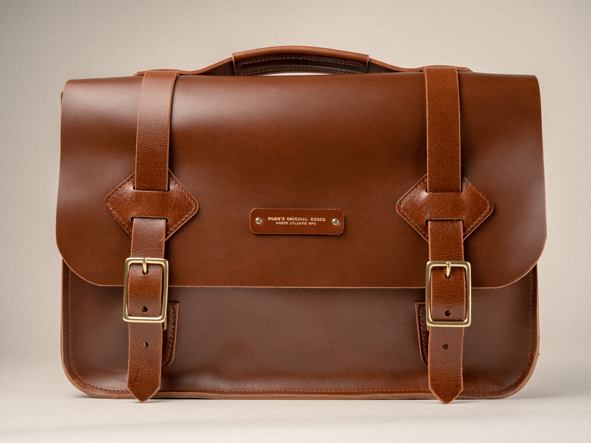 Chestnut brown leather satchel sitting on an off white background