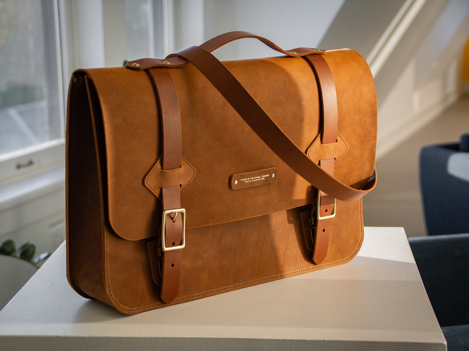 Glengarry messenger bag in wheat, sitting on a pedestal in an office showing shoulder strap.