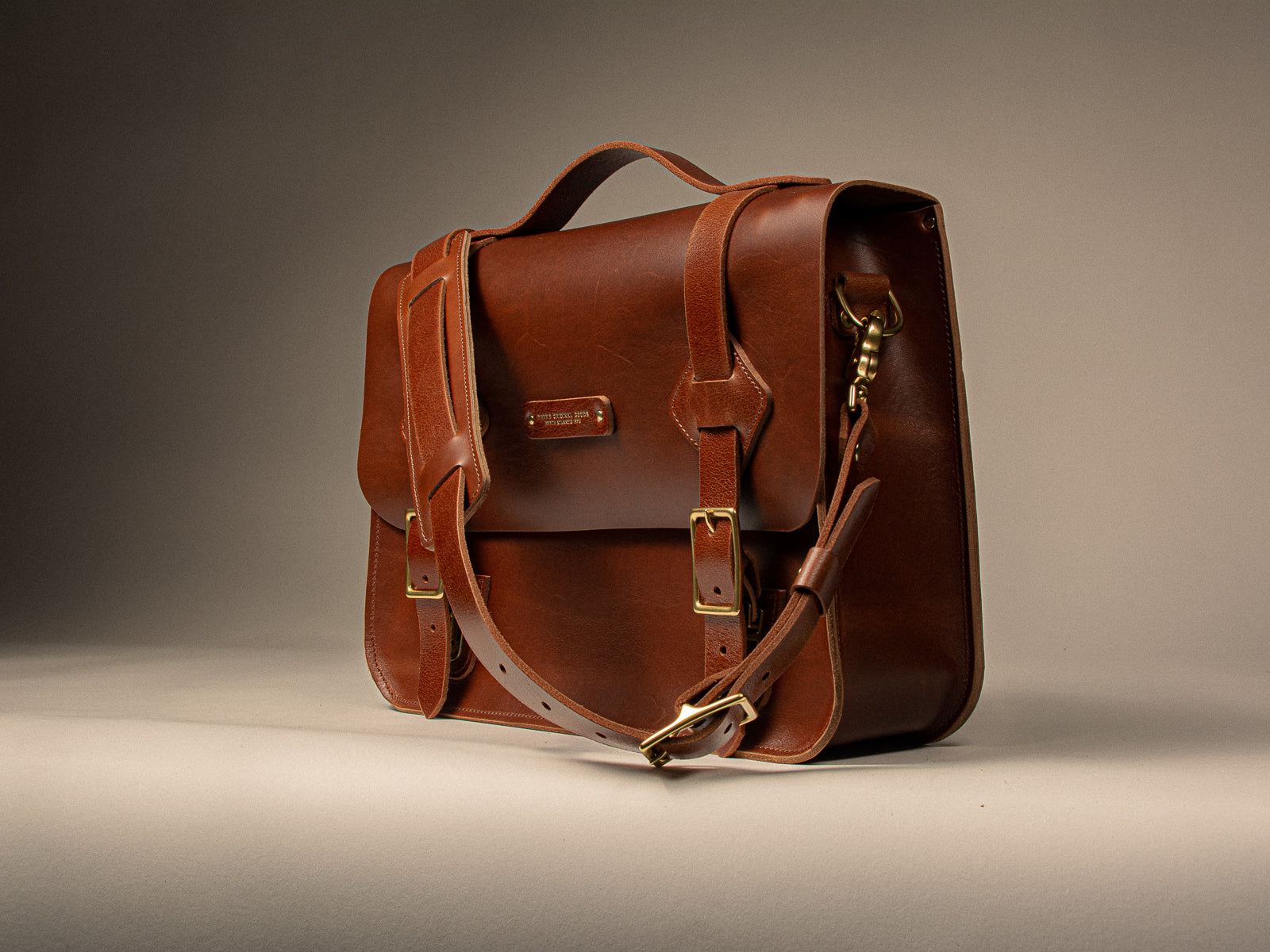 Chestnut brown leather satchel sitting on an off white background
