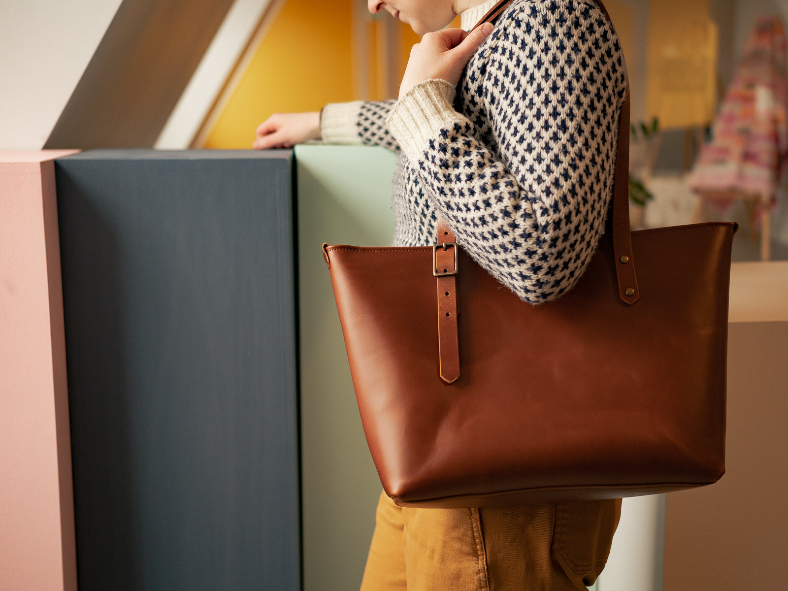 Person holding a tan Grand etang leather bag with adjustable strap