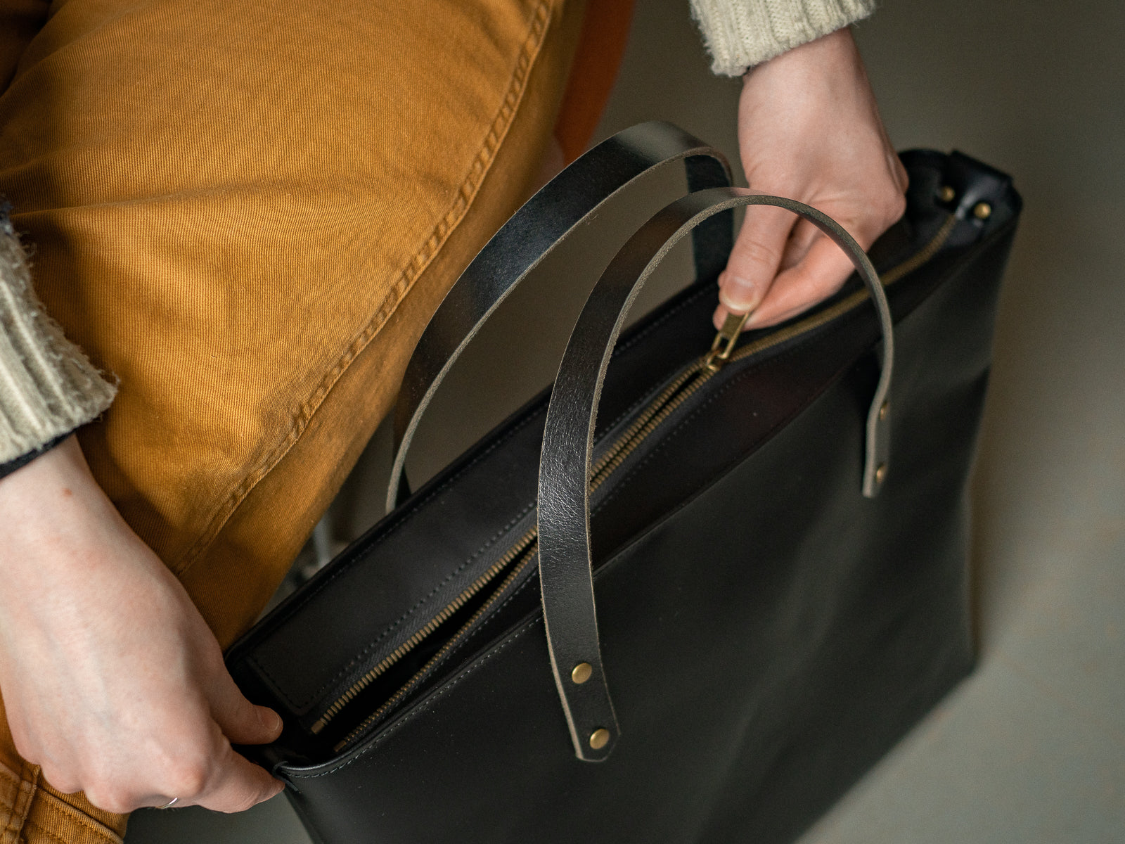 Person unzipping a black Grand Etang tote bag