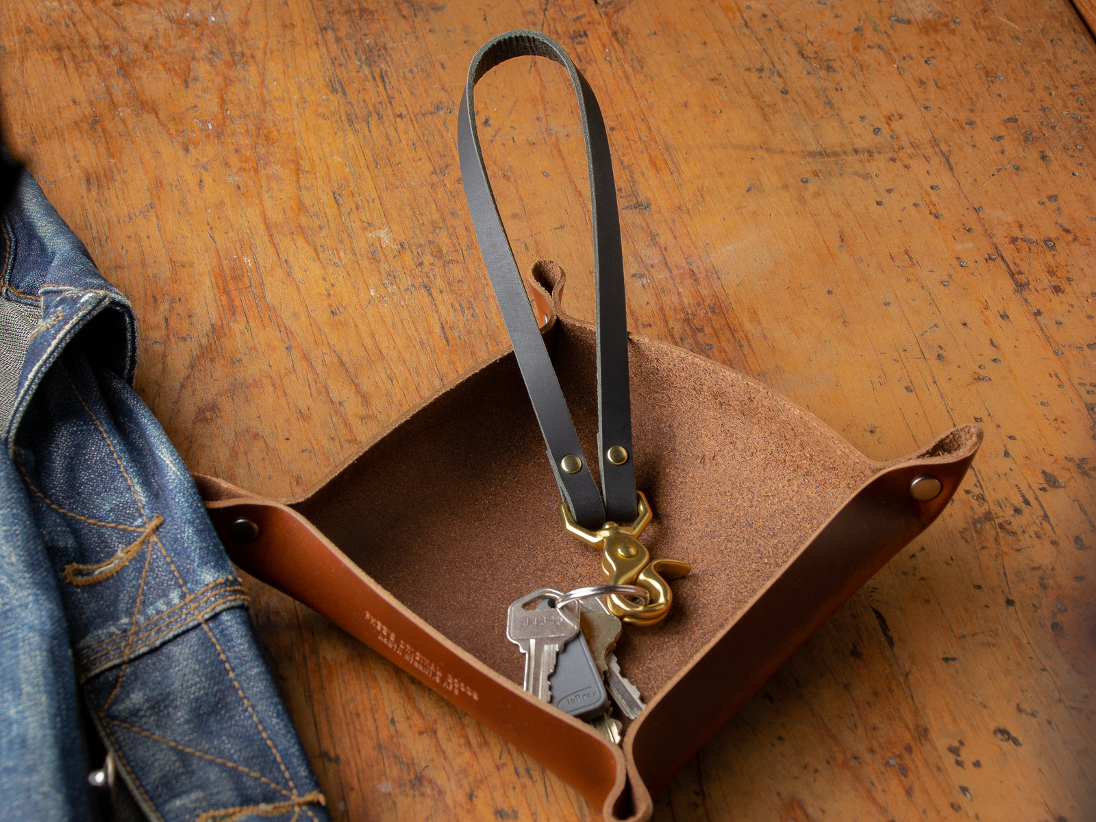 Black key lanyard sitting in valet tray on table beside denim jacket.