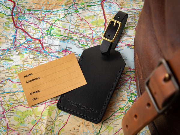 Black veg-tan leather luggage tag with brass secure buckle sitting on a map