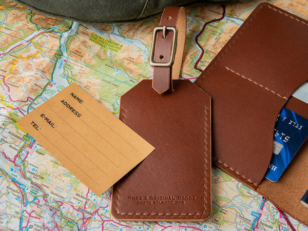 handmade leather luggage tag in brown veg-tan leather sitting with a travel wallet on map