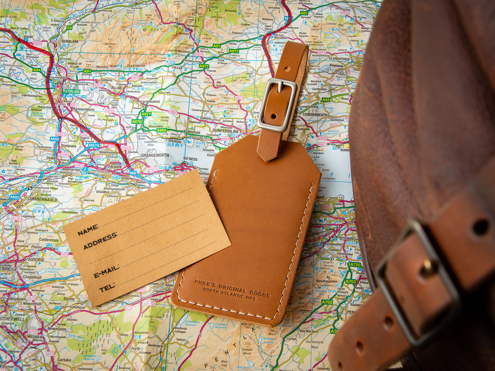 tan leather luggage tag, hand stitched with tapue thread sitting on a map