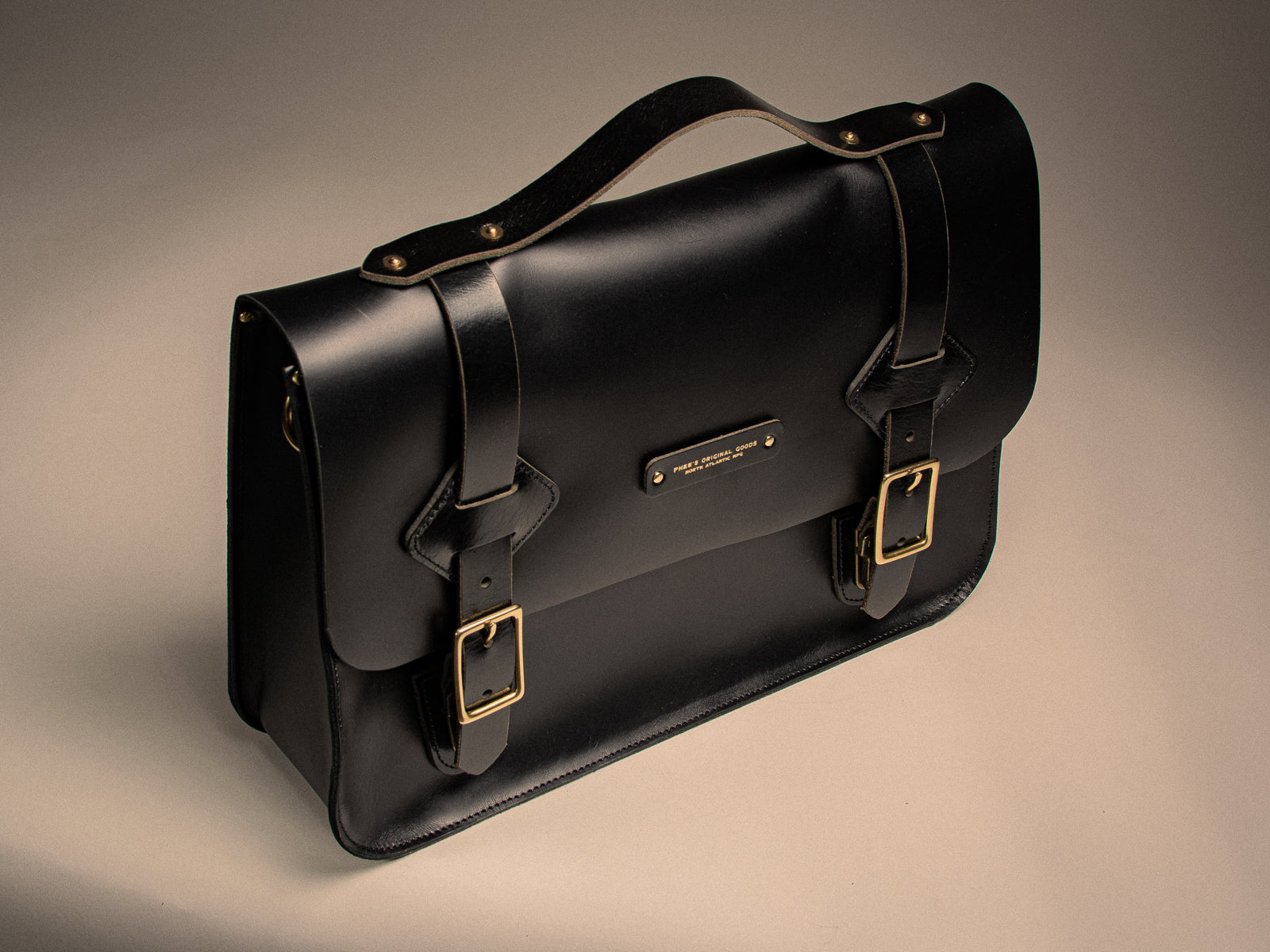 Black leather satchel with solid brass buckles on a beige background