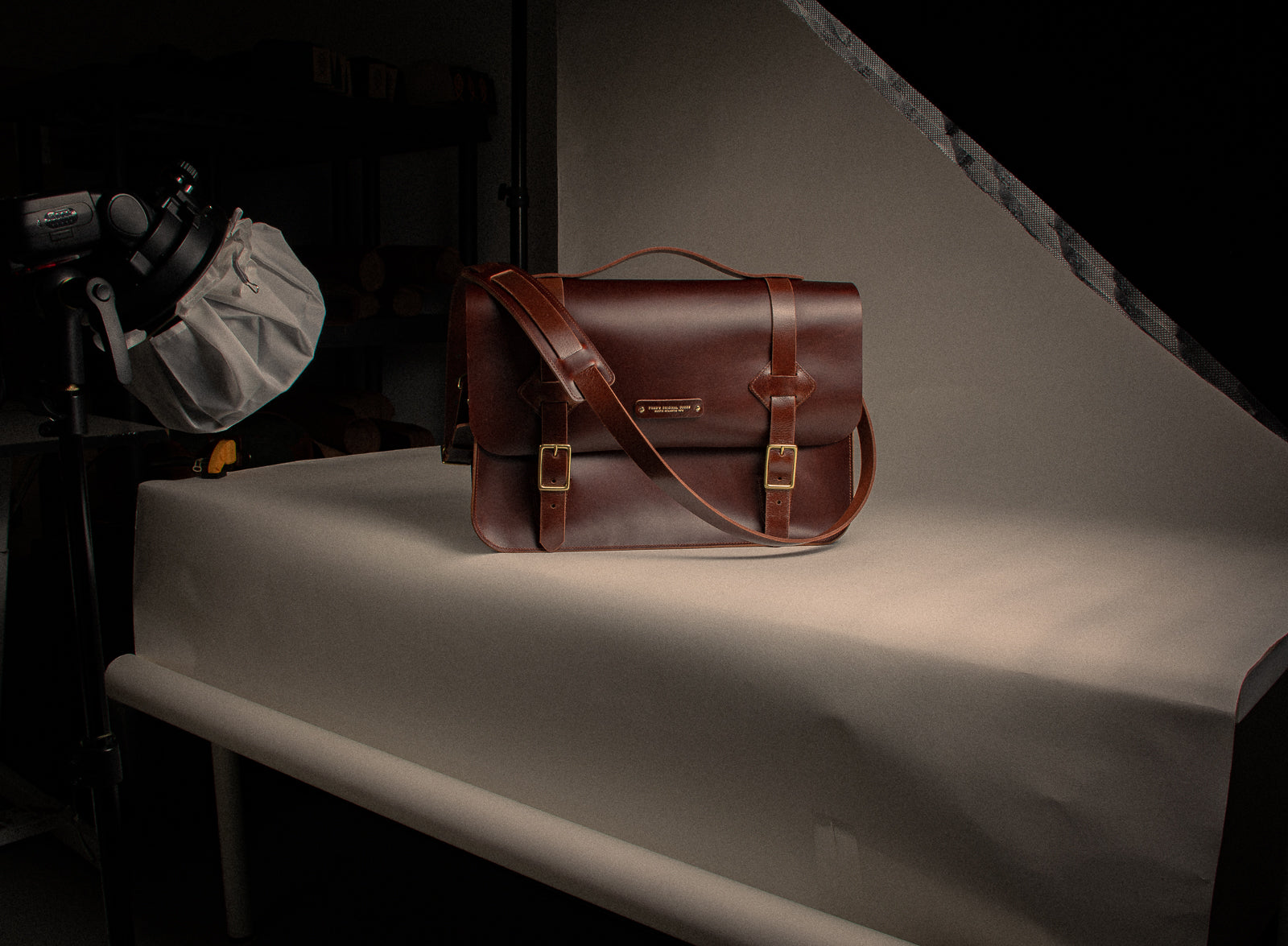 Brown leather satchel on a white surface with photography equipment in the background