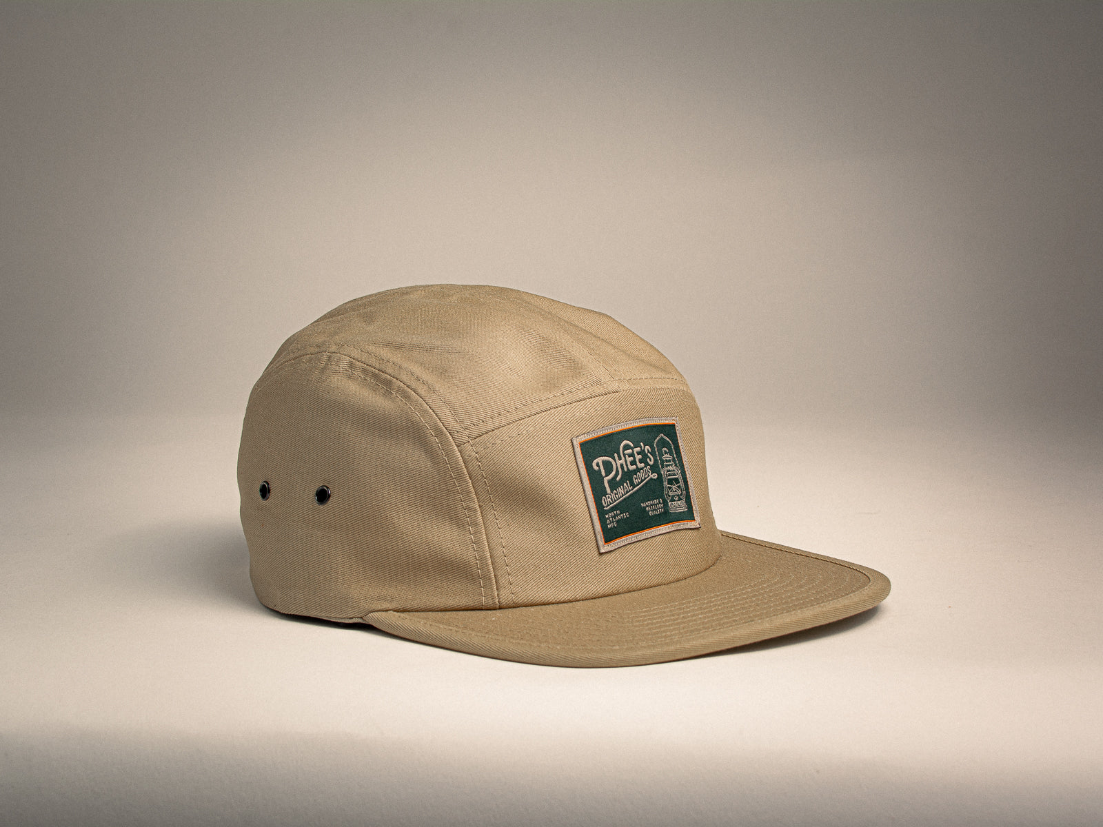 Khaki 5-panel hat with a woven label featuring an oil lamp sitting on a beige background