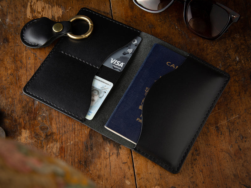 Black passport wallet sitting open on a table with air tag keychain