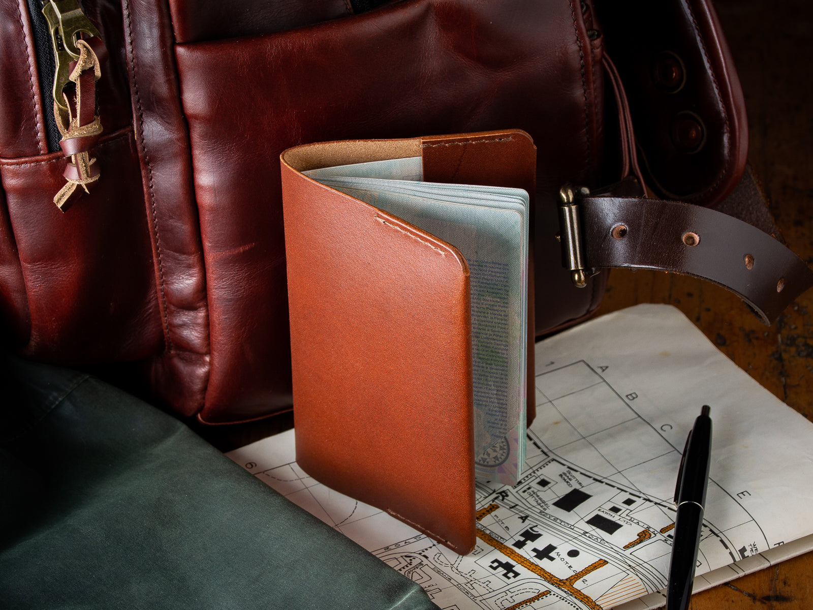 A brown passport Wallet sitting beside a backpack and map ready for an overseas trip