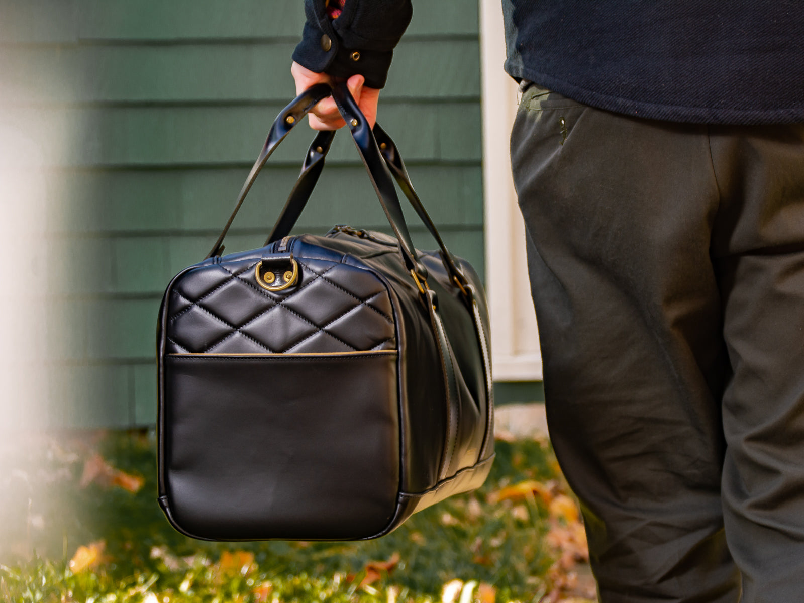 Black reserve duffel bag being held by a man's side walking into house.