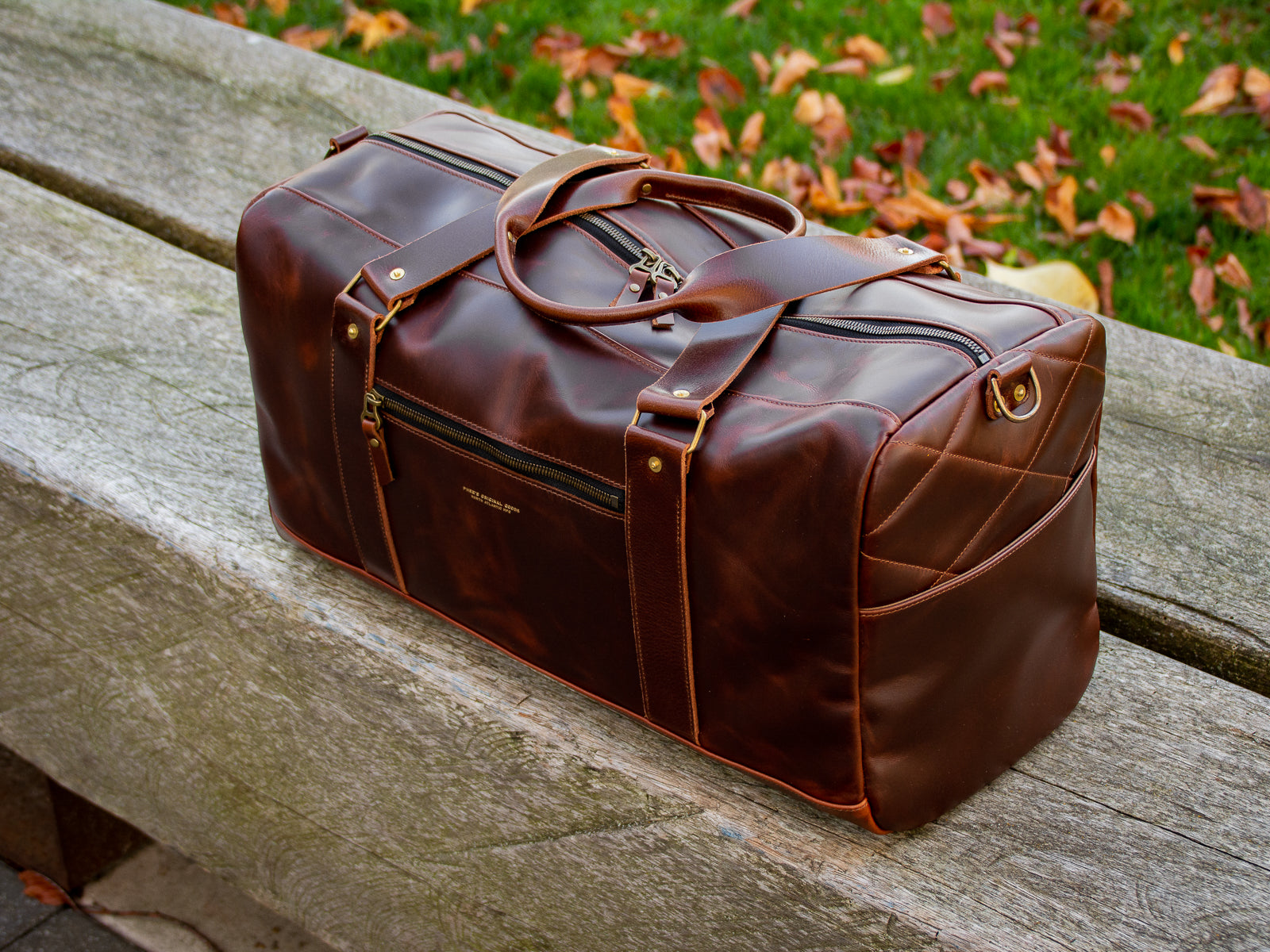 The reserve Duffel Bag in brown sitting on a wooden bench showing the quilted end panel and pocket.