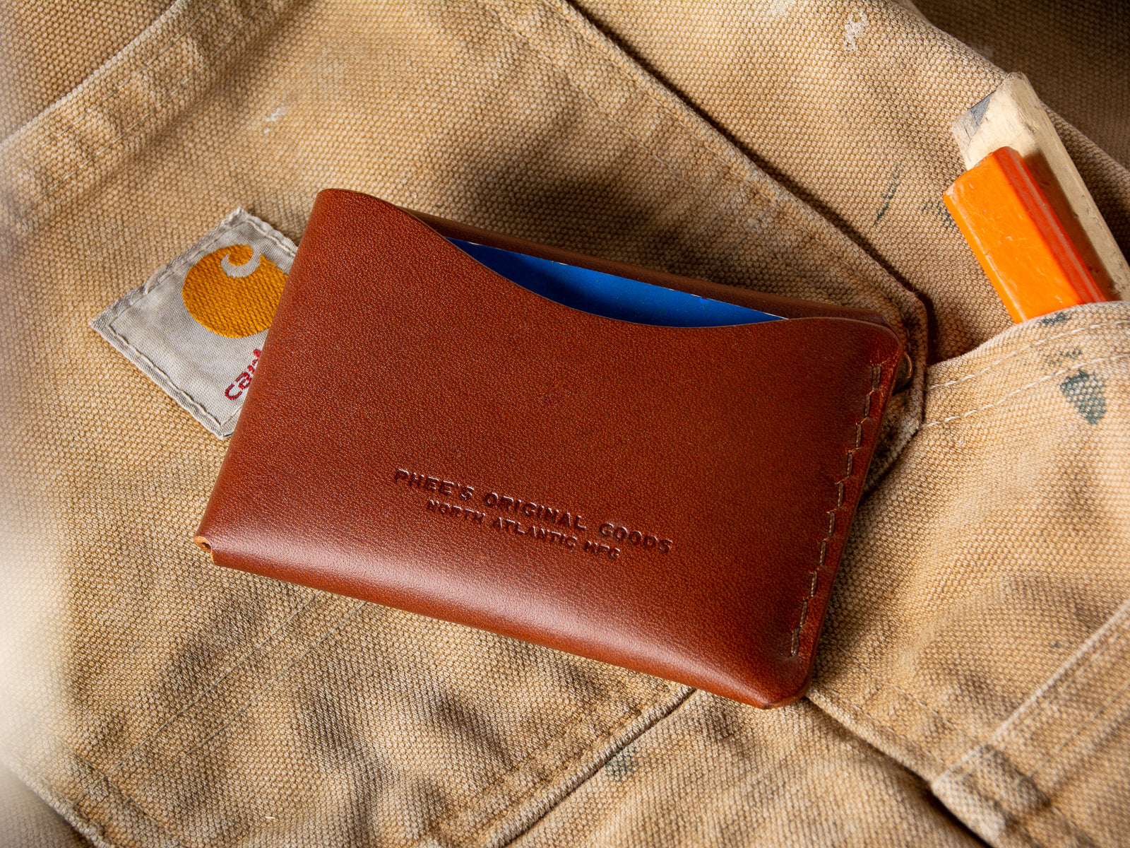 A brown Schooner card wallet sitting on a pair of Carhartt work pants