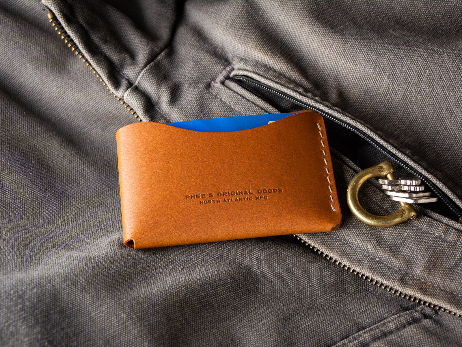 A tan Schooner fold wallet sitting beside a  Carhartt work vest pocket and keys