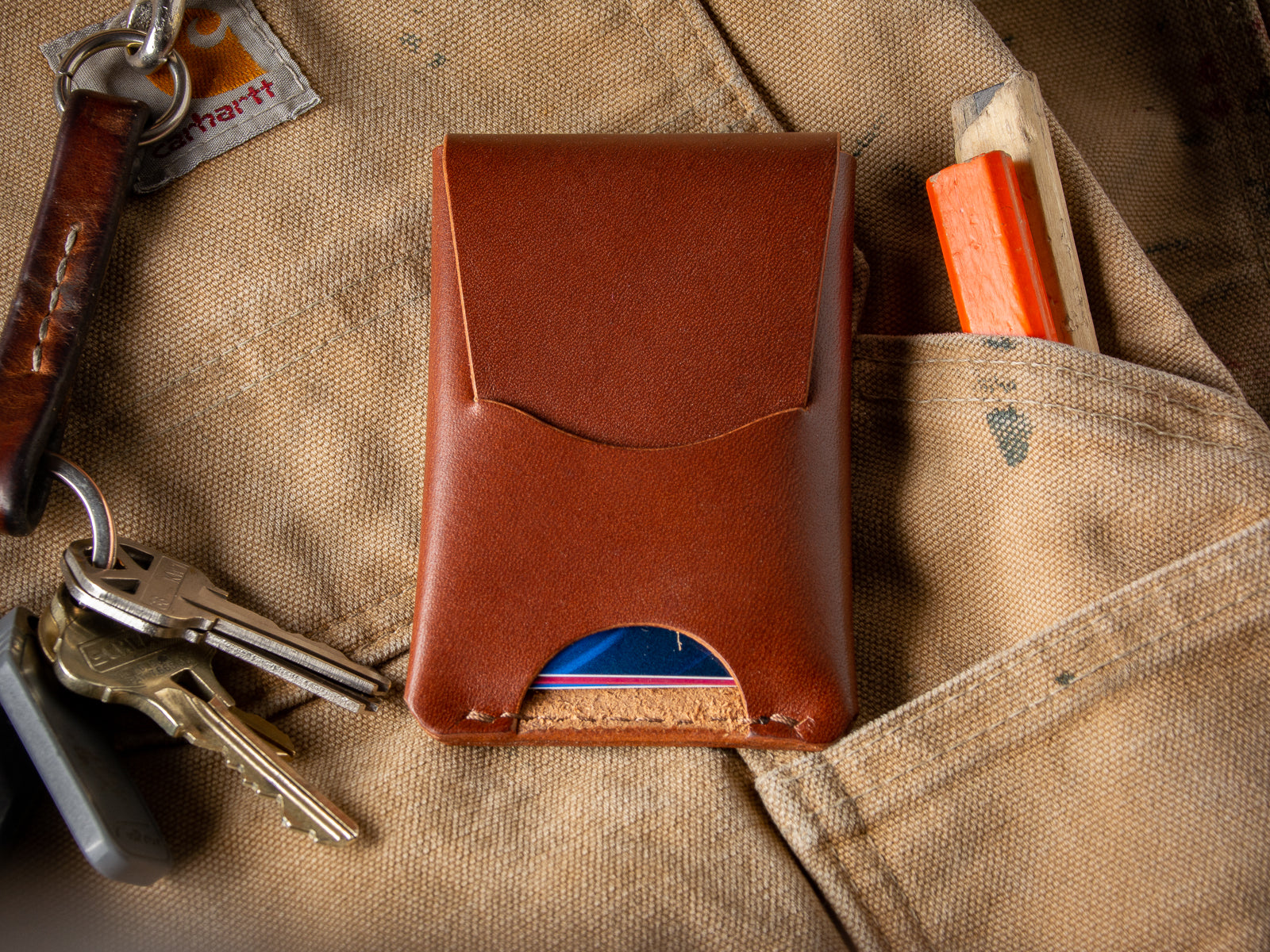 A brown Schooner card wallet sitting on a pair of Carhartt work pants