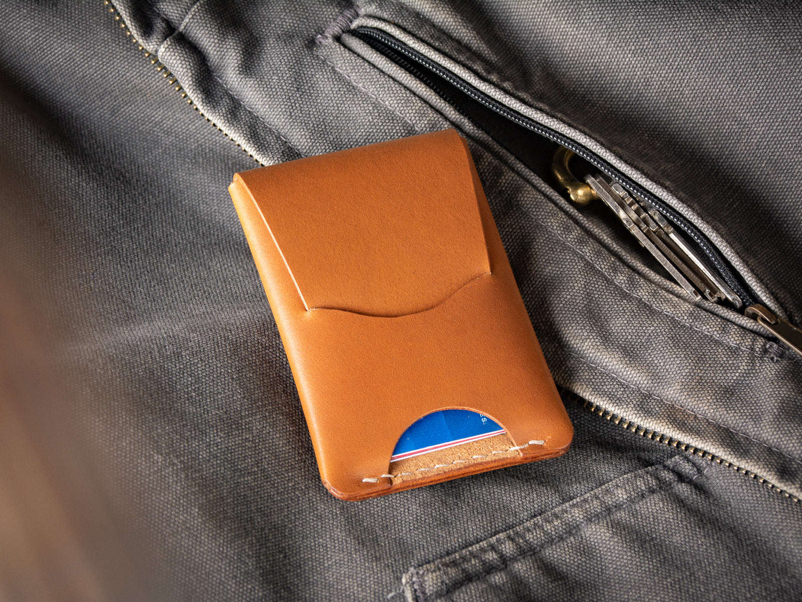 A tan Schooner fold wallet sitting beside a  Carhartt work vest pocket and keys