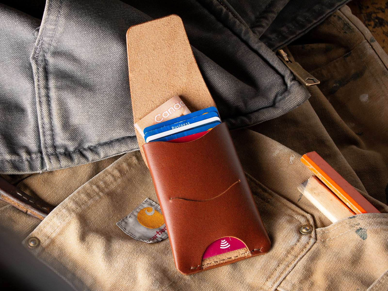 A brown Schooner card wallet sitting on a pair of Carhartt work pants