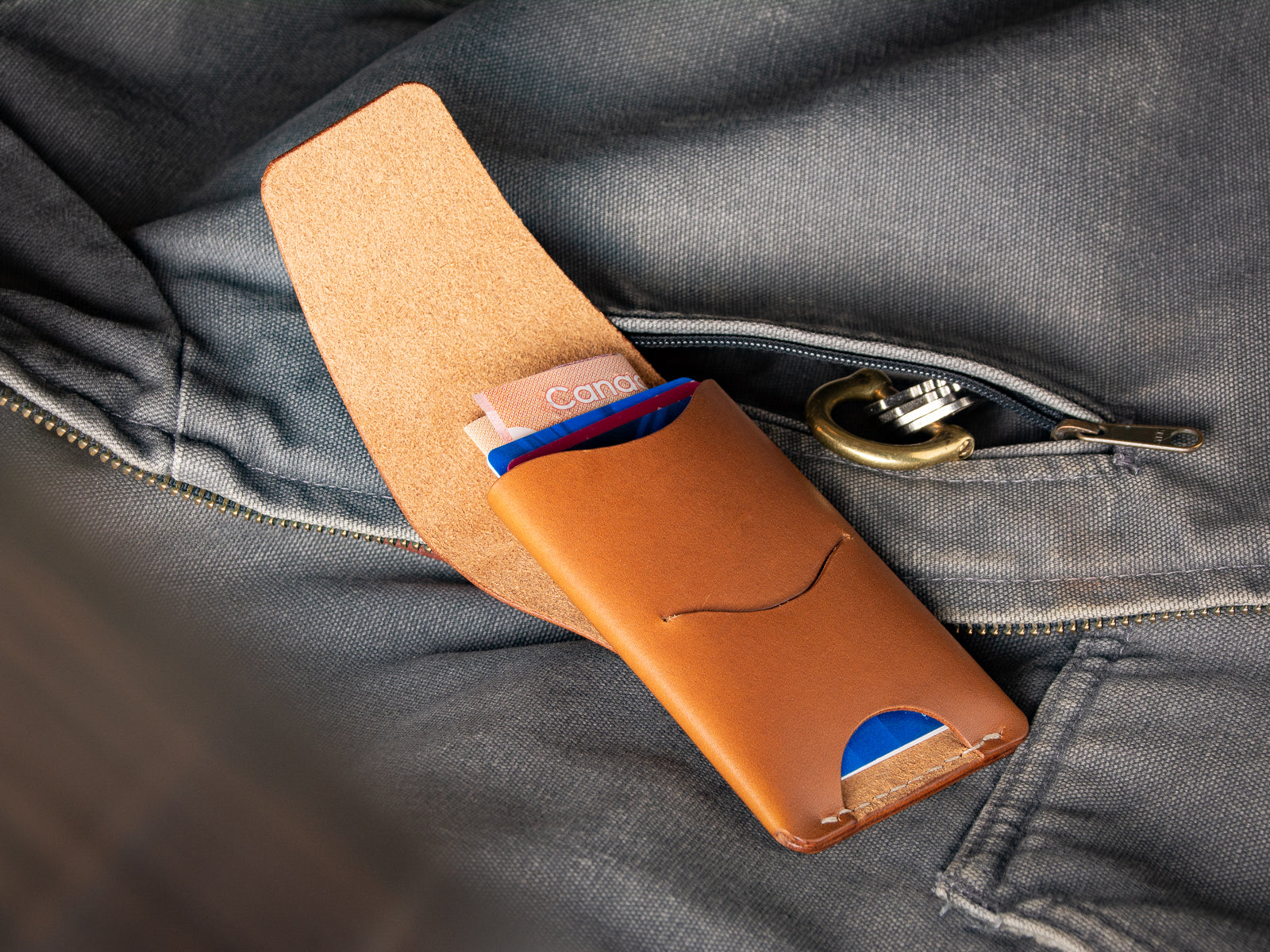 A tan Schooner fold wallet sitting beside a  Carhartt work vest pocket and keys