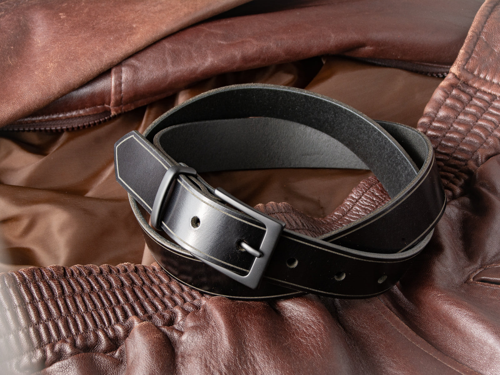 The Sterling Dress Belt in black shown coiled on a leather jacket with black buckle and keep.