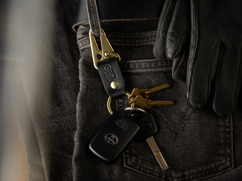 A black stubby keychain in full grain leather and brass hardware is clasped to a pair of LEvi's denims 