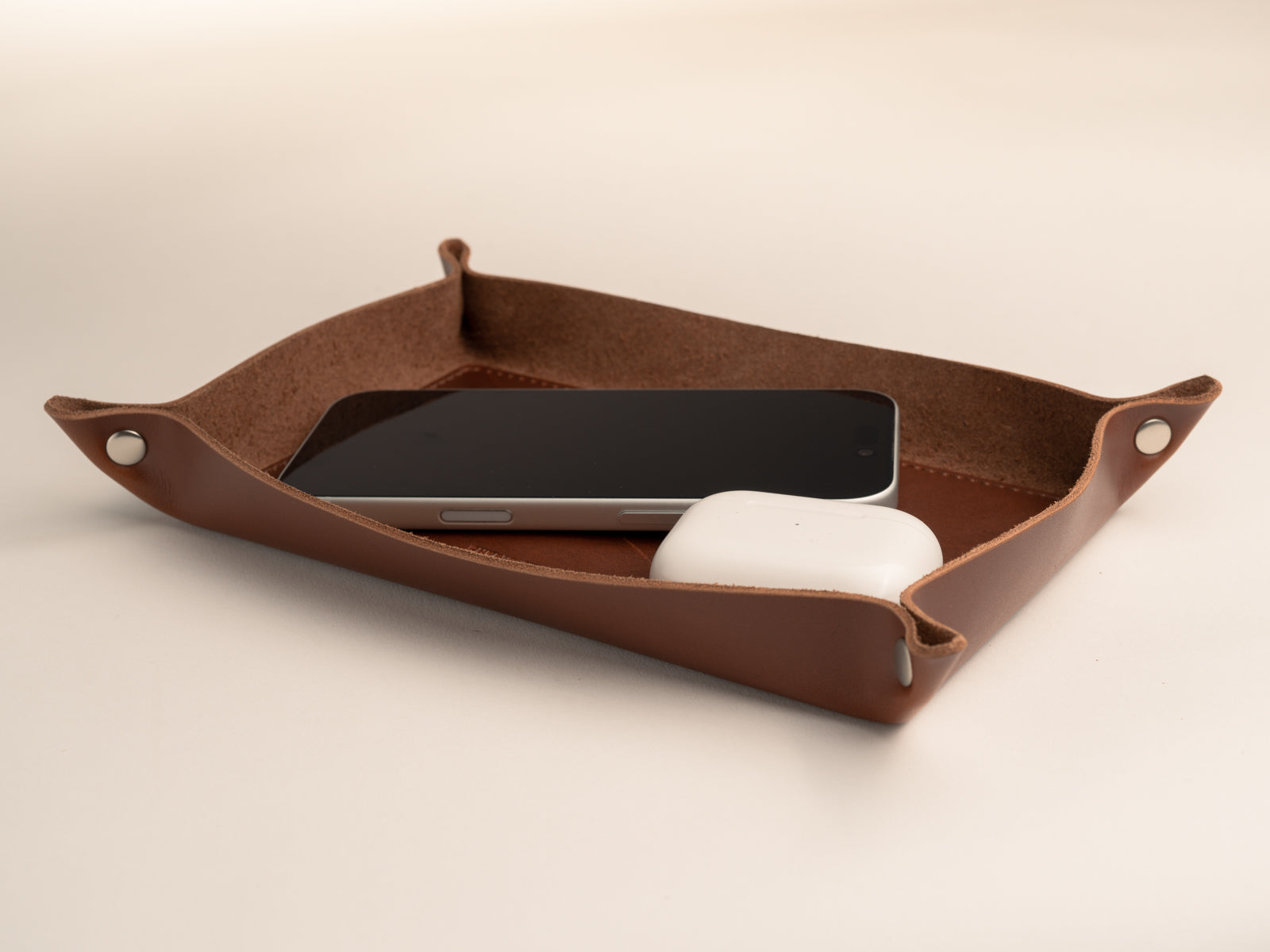 Handmade valet tray in tan leather with nickel finish solid brass rivets with iphone and airpods in it