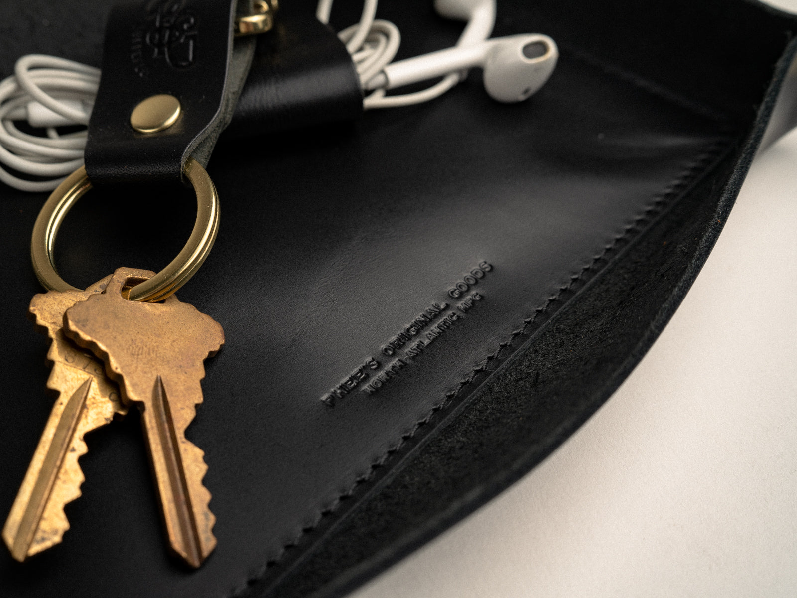 close up detail photo of black leather valet tray with keys and ear buds in it