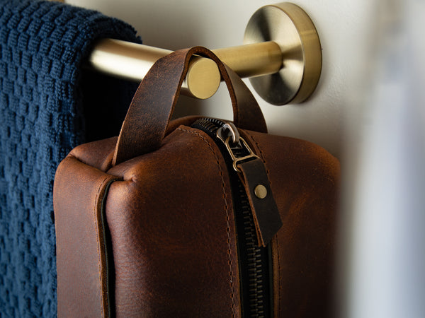 detail picture oil tan leather shaving kit with brass hardware hanging off a towel rail