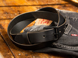 A black handmade Ashfield leather belt laying on top of a pair of Levi's Denim jeans.