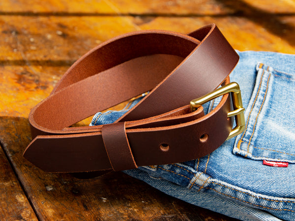 A brown handmade Ashfield leather belt laying on top of a pair of Levi's Denim blue jeans.