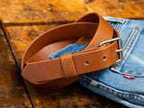 A tan handmade Ashfield leather belt laying on top of a pair of Levi's Denim blue jeans.