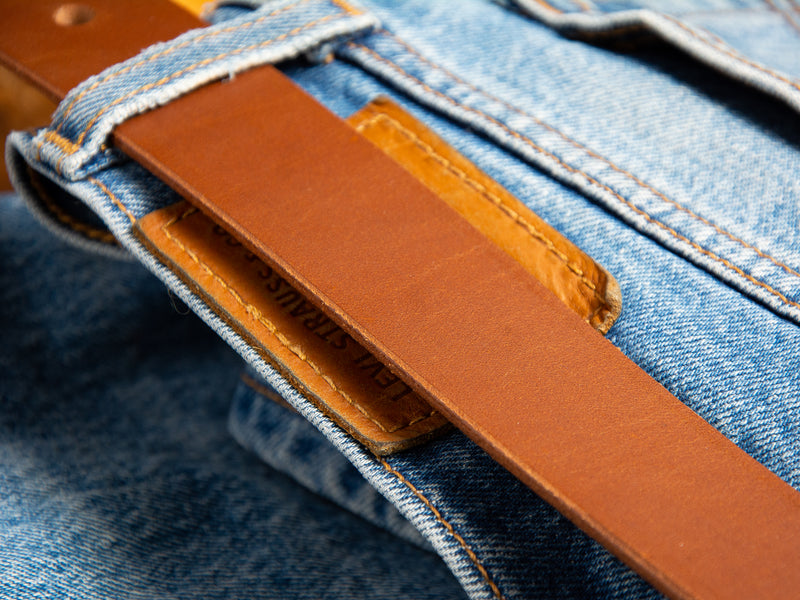 A tan Handmade Ashfield Leather Belt shown through belt loops on a pair of Levi's denim blue jeans.