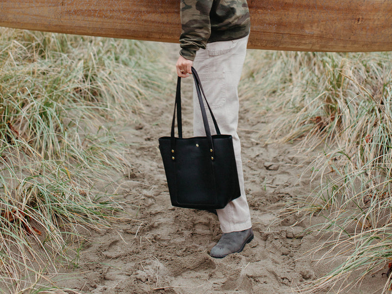 Person holding the black Big Bras d'Or leather purse, walking down a sandy path