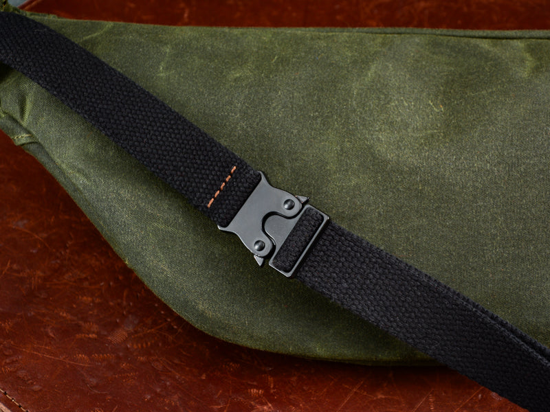 Detail photo of black cotton webbing and black metal clasp sitting on top of the back of the green fanny pack.