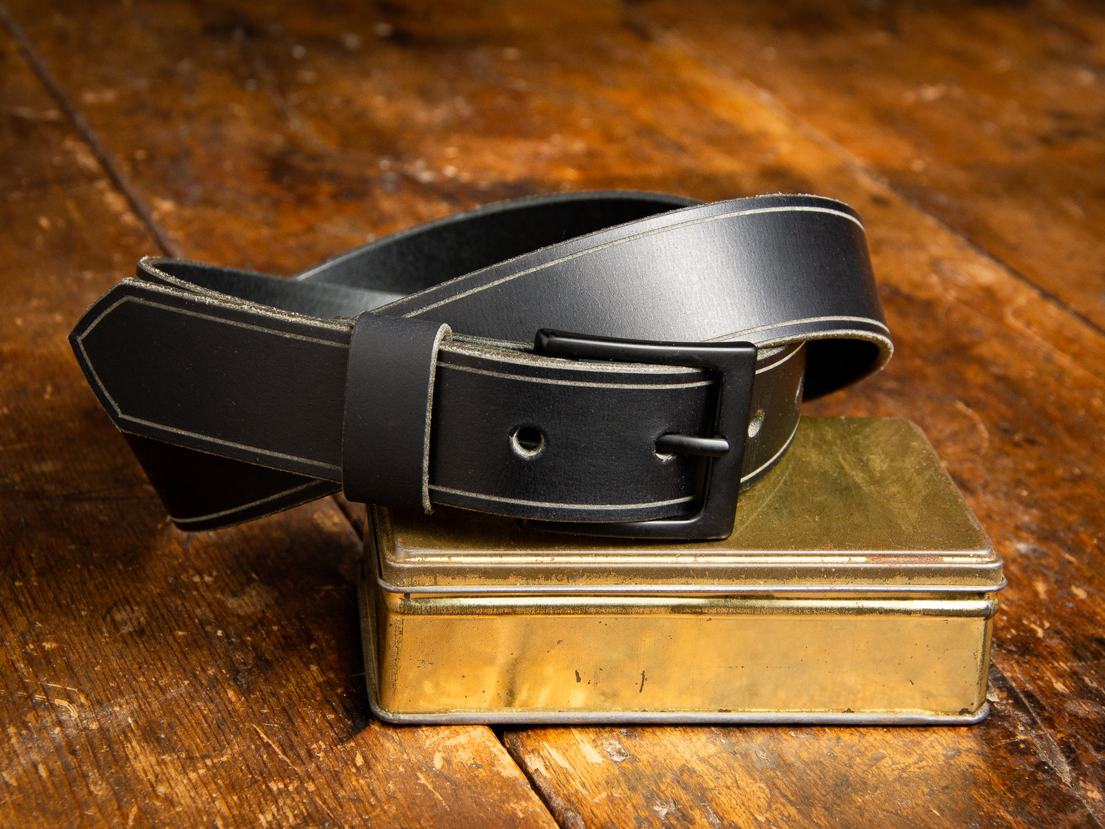 The Sterling Dress Belt in black shown resting on a brass tin.
