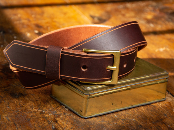 The Sterling Dress Belt in brown shown resting on a brass tin.