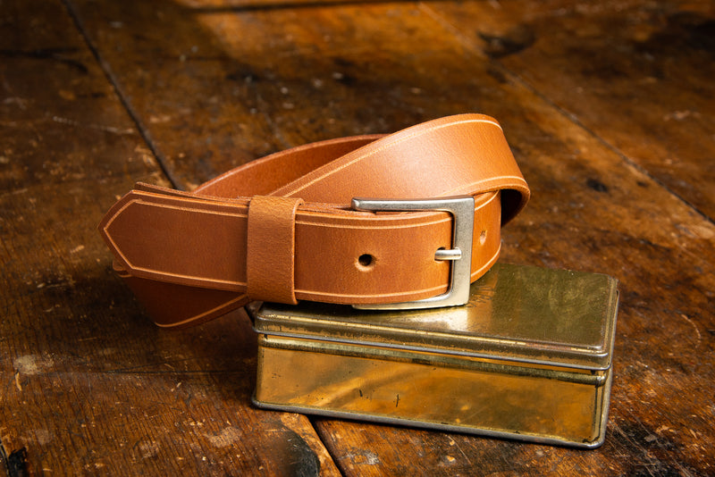 The Sterling Dress Belt in tan shown resting on a brass tin.