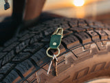 stubby leather keychain made with pine english bridle leather and solid brass hardware sitting on a tire